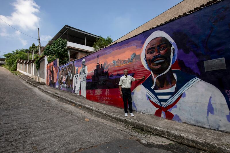 Adalberto poses beside a mural that depicts the story of his father Joao Candido, a sailor who led a revolt against the Brazilian Navy, in Sao Joao de Meriti, Brazil. Candido was one of only two mutineers to survive the subsequent torture. AP