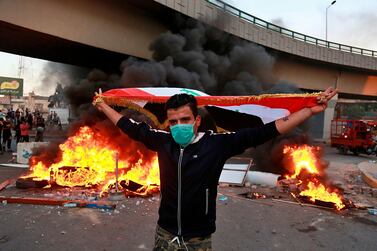 A protester holds an Iraqi flag while anti-government protests set fire while security forces fired live ammunition and tear gas near the state-run TV in Baghdad, Iraq, Monday, Nov. 4, 2019. (AP Photo/Khalid Mohammed)