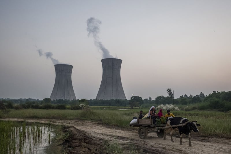 A cattle-pulled cart passes the central chimneys of the coal-fired power plant in India. Less developed and low-income economies are likely to bear bigger burden of energy transition. Bloomberg