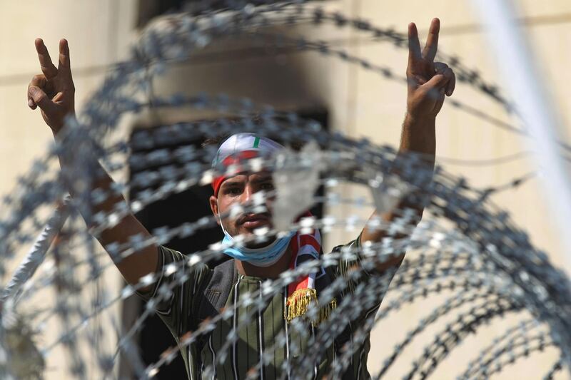 TOPSHOT - An Iraqi protester flashes the victory sign from behind barbed wire near the capital Baghdad's Al-Jumhuriyah Bridge on October 26, 2019, during an anti-government protest.  Iraqi security forces fired tear gas to clear lingering protesters in Baghdad this morning, after dozens died in a bloody resumption of anti-government rallies to be discussed in parliament. / AFP / -
