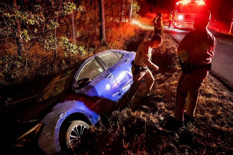 California Highway Patrol officers stand next to a car that crashed into a ditch as the driver attempted to flee from the fire in Mariposa county. AP