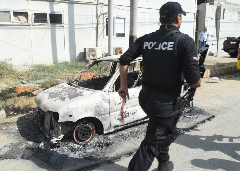 A Pakistani police commando walks past a burnt vehicle outside the Chinese consulate in Karachi. AFP