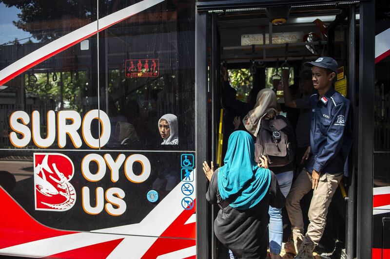 A bus conductor, right, looks on as passengers board a Suroboyo bus.