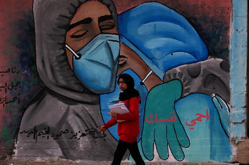 A student walks past a mural encouraging the wearing of face masks with the words "protect yourself" written in Arabic, on the main road of Nusseirat refugee camp, central Gaza Strip. AP Photo