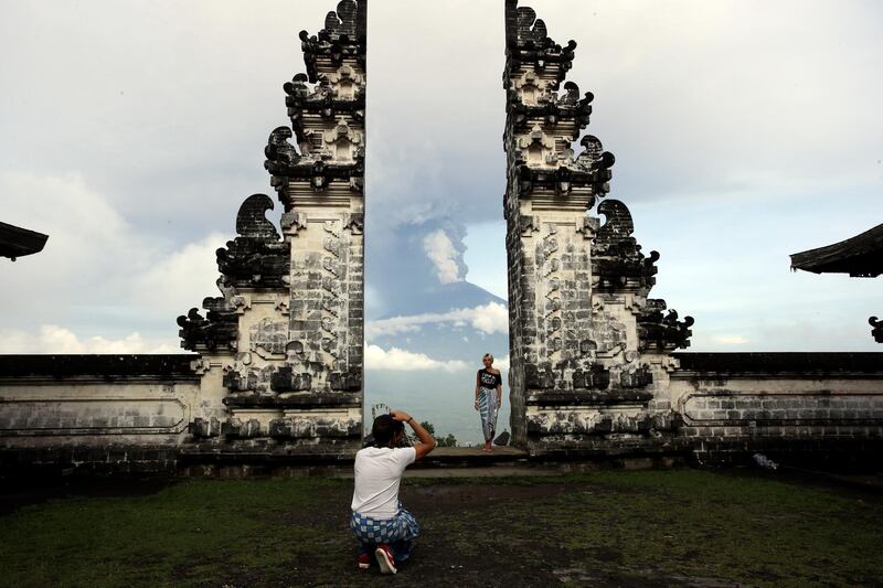 A tourist poses for a photo with Mount Agung volcano erupting as they visit a temple in Karangasem, Indonesia. Firdia Lisnawati / AP Photo