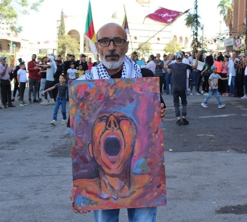 Suhail Thebian, a Syrian painter and former political prisoner, holds a painting by a fellow artist at a demonstration in the south-western province of Suweida. Photo: Suhail Thubian