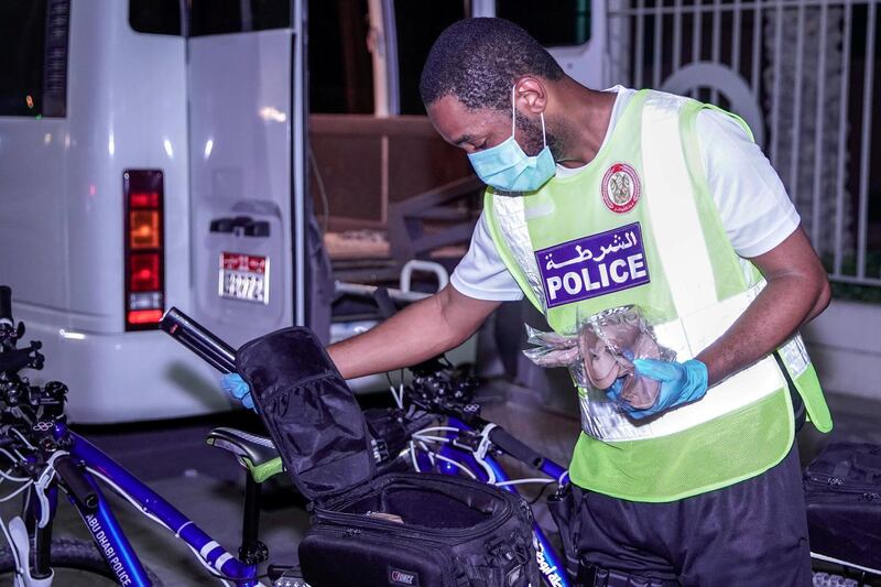 Abu Dhabi, United Arab Emirates, May 11, 2020.   Abu Dhabi Police bicycle patrol do night operations around the Mussaffah area to warn or catch curfew violators in the residential areas.  --  A bike patrol police officer loads the duffle bags of the bikes with face masks and gloves to give residents without coronavirus protective gear in the neighborhood.
Victor Besa / The National
Section:  NA
Reporter:  Haneen Dajani
