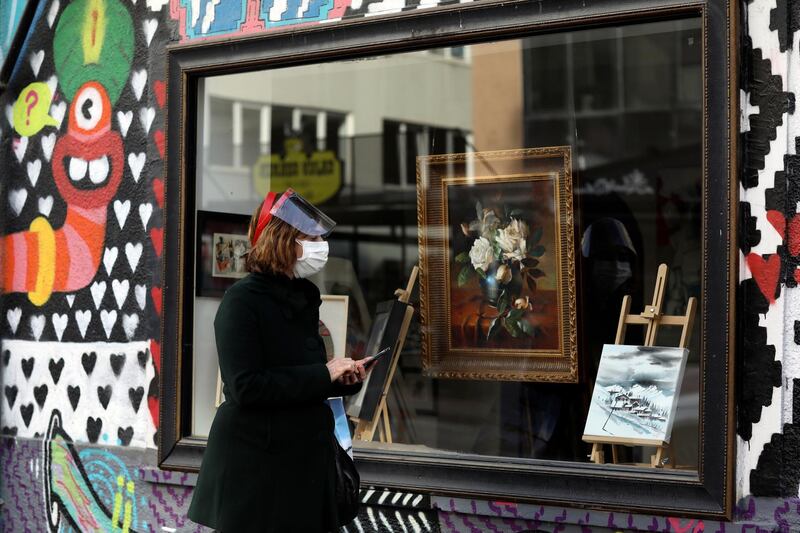 Semure Aras, wearing a mask to help protect against the spread of coronavirus, watches paintings displayed at the window of an art gallery, in Ankara, Turkey, Tuesday, Feb. 2, 2021. Turkey said last week it has detected the more infectious COVID-19 variant that was first found in southeast England, in 17 cities across the country. (AP Photo/Burhan Ozbilici)