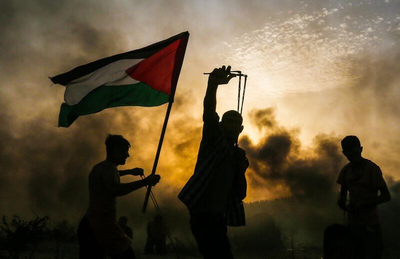 A Palestinian protester holds a national flag as another protester throws a stone towards Israeli forces during a demonstration on the beach near the maritime border with Israel, in the northern Gaza Strip. AFP Photo