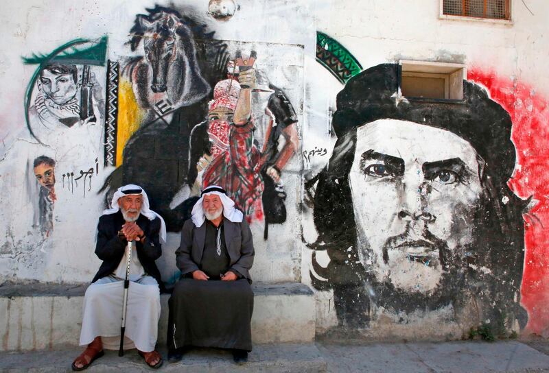 A Palestinian elder sits next to his neighbour in front of a mural depicting a protester firing a slingshot next to another showing Argentine-born revolutionary leader Ernesto "Che" Guevara, on a wall in al-Aroub Palestinian refugee camp, between the West Bank towns of Hebron and Bethlehem.  AFP