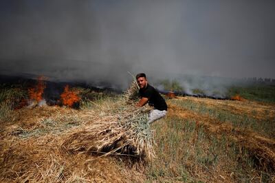 A man moves a bundle of wheat as a fire burns on a field after a rocket launched from the Gaza Strip landed near homes in Moshav Zohar, Israel May 13, 2021. REUTERS/Amir Cohen