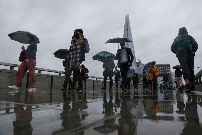 Commuters use their umbrellas to shelter from the rain as they cross London Bridge in London, U.K., on Monday, June 21, 2021. Almost half of London companies whose staff can work from home expect them to do so up to five days a week after the pandemic finishes, and smaller businesses are more likely than larger ones to move ahead with remote working. Photographer: Hollie Adams/Bloomberg