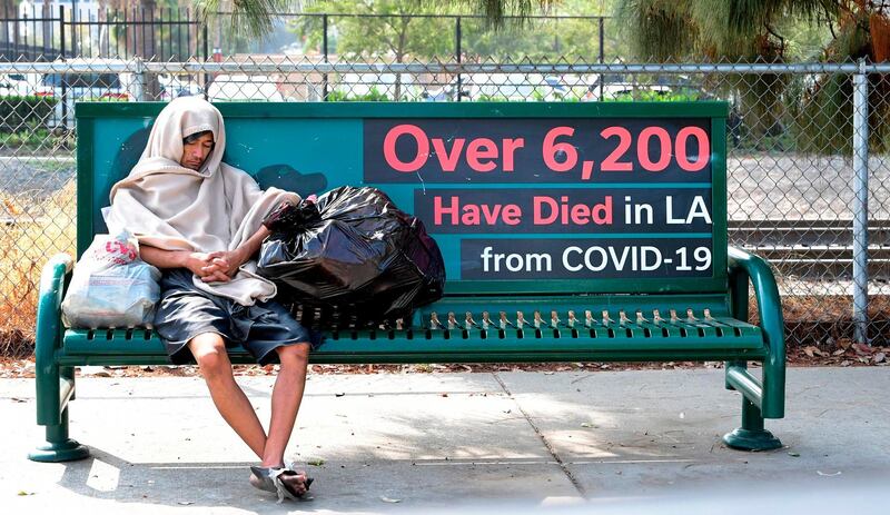 A homeless person naps on a street bench reading "over 6,200 have died in LA from Covid-19", in Los Angeles, California. AFP