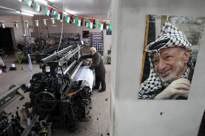 Palestinian Yasser Al Hirbawi, the owner of the Palestinian factory which produces kaffiyeh, stands behind a portrait of Yasser Arafat. AFP Photo