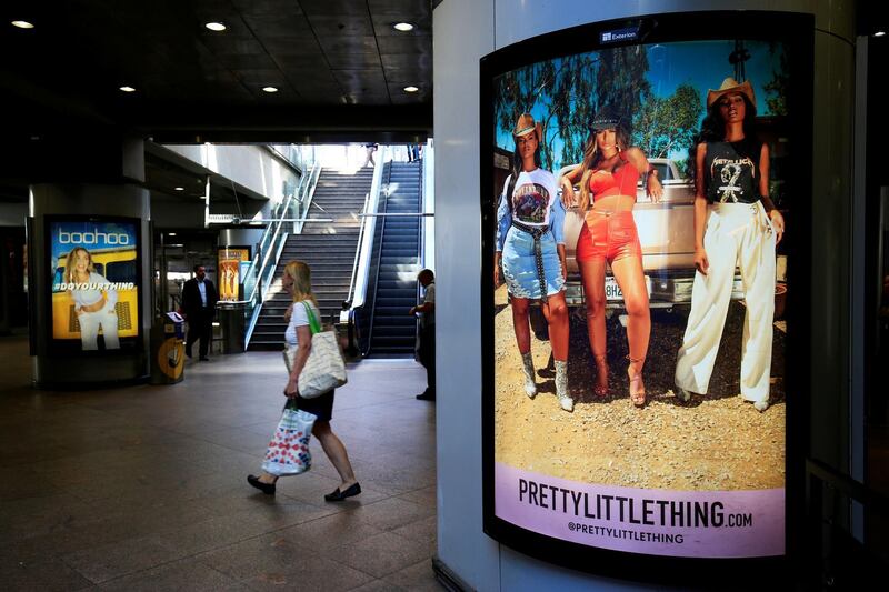 A shopper walks pass advertising billboards for Boohoo and for 'Pretty Little Things', a Boohoo brand, at Canary Wharf DLR station in central London, Britain. REUTERS