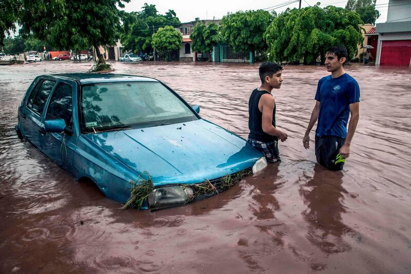 Young men wade next to a car in a flooded street in Culiacan, Sinaloa State, Mexico.  AFP