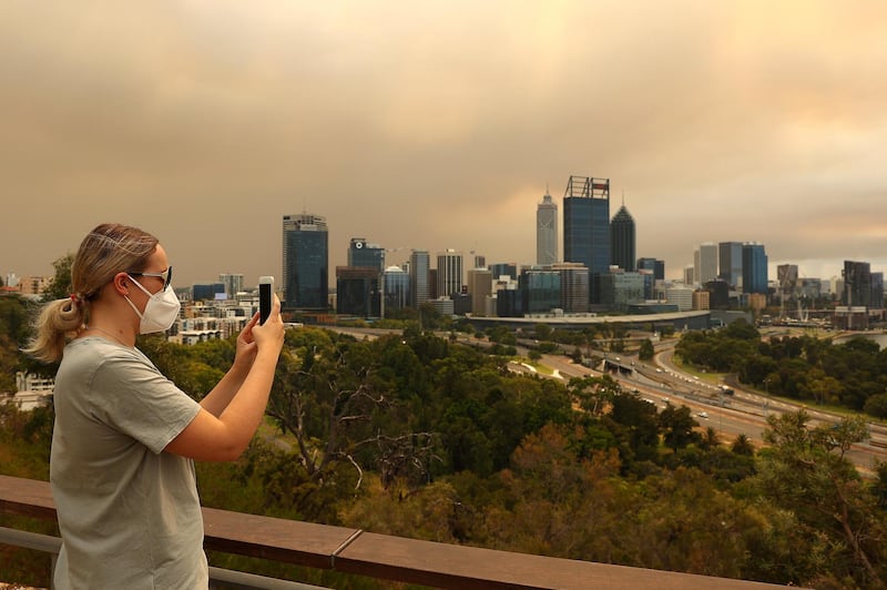 A local resident takes a panoramic image of the bush fire and Perth CBD on her phone from Kings Park. Getty Images