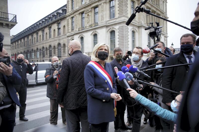 French far-right leader Marine le Pen, center, wearing a protective face mask, talks to media after laying a wreath during a ceremony Saturday, May 1, 2021 in Paris. Far-right militants usually gather at the statue for their annual May Day march. (AP Photo/Thibault Camus)