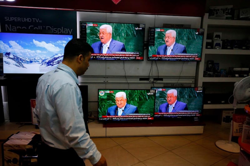 A walks past screens of TVs for sale showing Palestinian president Mahmoud Abbas in  West Bank city of Ramallah. AFP