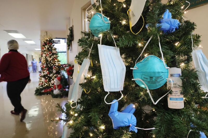 MISSION HILLS, CALIFORNIA - DECEMBER 24: A caregiver walks past a Christmas tree decorated with face masks, hand sanitizer and other PPE at the Ararat Nursing Facility on Christmas Eve on December 24, 2020 in Mission Hills, California. Due to the COVID-19 pandemic, family members are not allowed to visit relatives inside the facility but are able to hold personal visits at a window at the facility.   Mario Tama/Getty Images/AFP
== FOR NEWSPAPERS, INTERNET, TELCOS & TELEVISION USE ONLY ==
