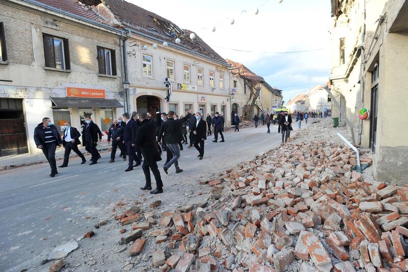 Croatian President Zoran Milanovic, sixth left, and Prime Minister Andrej Plenkovic, seventh left, walk past damaged buildings in Petrinja, Croatia.  AP