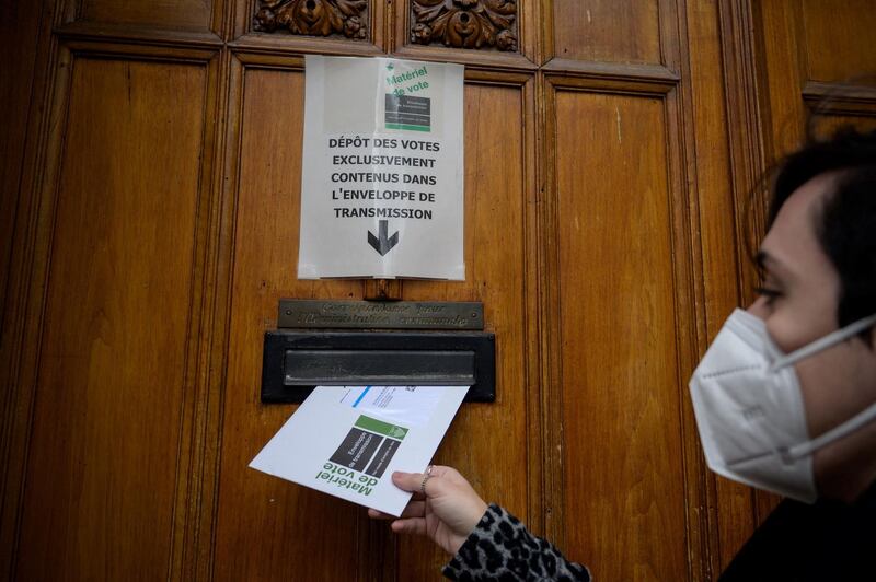 A woman wearing a facemask as a preventive measure against the Covid-19 coronavirus casts an envelope containing her ballot during a vote by correspondence during a day of national referendum and local election on March 7, 2021 in Lausanne. Switzerland votes on March 7, on whether to ban full facial coverings in public places, despite women in Islamic full-face veils being an exceptionally rare sight in Swiss streets. Two other votes are also being held, one is on the free trade agreement struck between Switzerland and Indonesia, the other vote is on a government plan to introduce a federally recognised electronic identity, that could be used for ordering goods and services online. / AFP / Fabrice COFFRINI
