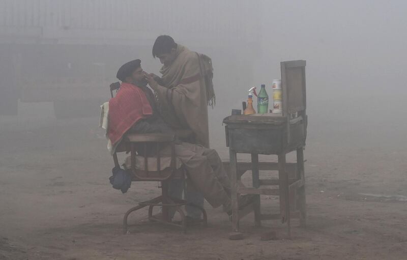 A Pakistani barber shaves a customer alongside a road amid heavy fog and smog in Lahore. AFP