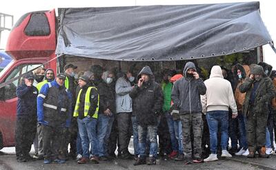 Drivers shelter from the rain by a lorry as they block the road by the entrance to the port in Dover, in Kent, south east England on December 23, 2020, as they are not being allowed to enter by police after the UK and France agreed a protocol to reopen the border to accompanied freight arriving in France from the UK.  France and Britain reopened cross-border travel after a snap 48-hour ban to curb the spread of a new coronavirus variant threatened UK supply chains. Accompanied frieght will now be allowed to cross the channel from the port of Dover but all lorry drivers will require a lateral flow test and a negative Covid-19 result before the travel.
 / AFP / JUSTIN TALLIS
