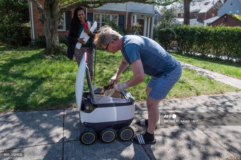 Kimmo Kartano unloads a food delivery robot from the Broad Branch Market grocery store as Audra Grant looks on in front of their house in the Chevy Chase neighborhood of Washington, DC, on April 9, 2020. - The store began using the robots about two weeks ago and makes 10-15 deliveries a day within a limited area of the neighborhood. (Photo by NICHOLAS KAMM / AFP)