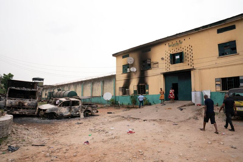 People walk past burned vehicles in front of a correctional facility in Owerri, Nigeria. Hundreds of inmates escaped from the prison in southeastern Nigeria after a series of coordinated attacks according to government officials. AP Photo