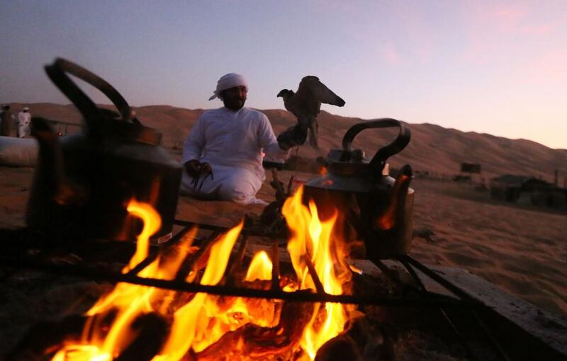 An Emirati from the Qubaisi tribe sits next a fire after training his falcon during the Liwa Moreeb Dune Festival.