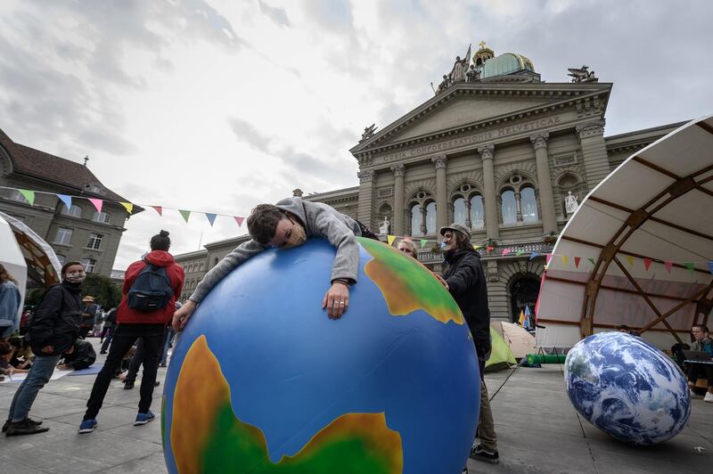 A climate activist lays on an inflatable world globe in front of the Swiss House of Parliament at the start of a week of demonstrations called "Rise up for change" on September 21, 2020 in Bern.   / AFP / Fabrice COFFRINI
