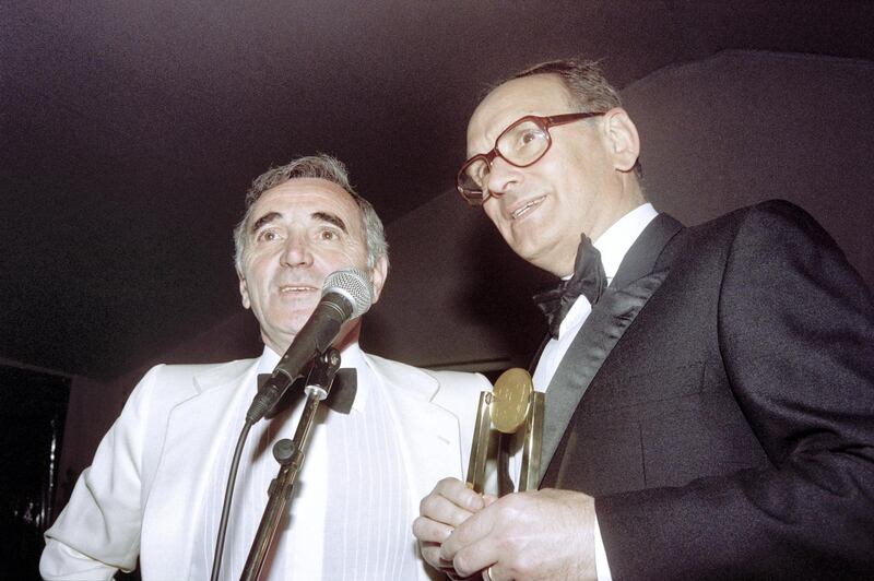 Italian composer Ennio Morricone (R) receives from French singer Charles Aznavour the Sacem music foundation's film score award during the 43th Cannes Film Festival on May 16, 1990 in Cannes. (Photo by Patrick KOVARIK / AFP)