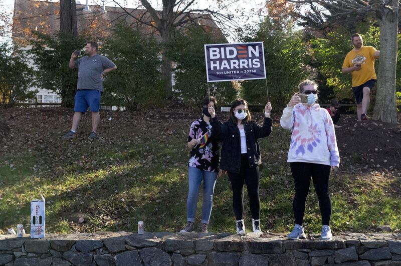 A person wearing a protective mask holds a 'Biden Harris' campaign sign outside Trump National Golf Club in Sterling, Virginia. Bloomberg