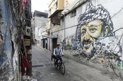 Mohammed, a Lebanese roaming barber, better known as "Abo Tawila", rides his bicycle in a street on the outskirts of the Palestinian refugee camp Burj al-Barajneh, south of the capital Beirut on May 29, 2018. On the wall is a mural painting of the late Palestinian leader Yasser Arafat. - Inspired by roaming street vendors in Beirut, 18 years-old Abo Tawila (the tall one in Arabic), decided to use his bicycle to set up his business. He works mainly in popular neighbourhoods in Beirut and its souther suburbs. (Photo by JOSEPH EID / AFP)