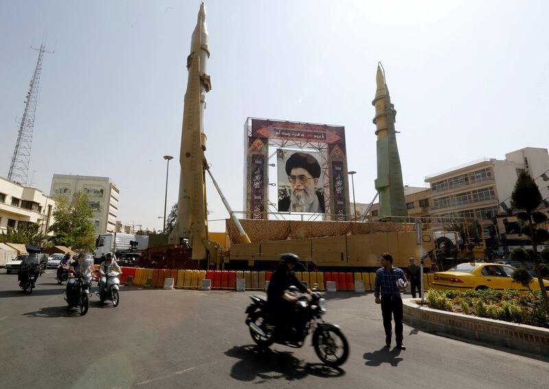 Iranians walk past Sejjil (L) and Qadr-H medium range ballistic missiles displayed next to a portrait of Iranian Supreme Leader Ayatollah Ali Khamenei on the occasion of the annual defence week which marks the anniversary of the 1980s Iran-Iraq war, on September 25, 2017, on Baharestan square in Tehran. / AFP PHOTO / ATTA KENARE
