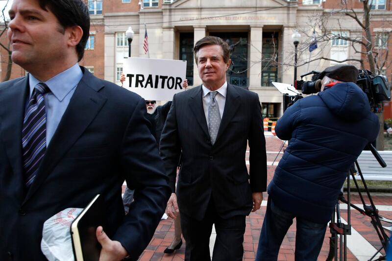FILE - In this March 8, 2018, file photo, Jason Maloni, left, former Trump campaign chairman Paul Manafort's spokesman, left, walks with Paul Manafort, center, as they leave the Alexandria Federal Courthouse after an arraignment hearing in Alexandria, Va. A federal judge in Virginia has rejected Manfort's move to throw out charges brought by the special counsel in the Russia investigation. The decision June 26 was a setback for Manafort in his defense against numerous tax and bank fraud charges. Behind Manafort protester Bill Christeson holds up a sign that says "traitor." (AP Photo/Jacquelyn Martin)