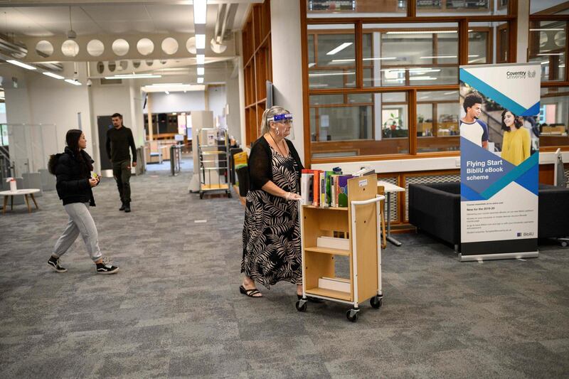 A member of library staff wearing a face visor pushes a book trolley through the library. AFP