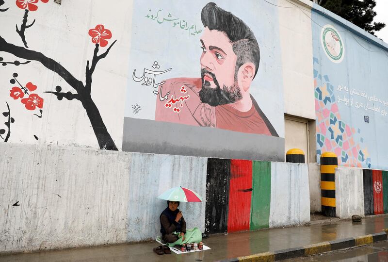 A shoe polisher boy holds an umbrella as he waits for customers under graffiti on a wall in Kabul, Afghanistan April 15. Reuters