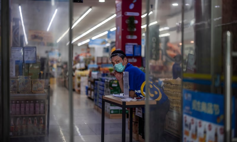 An employee stands at the entrance of a supermarket to check visitors' health app QR codes and body temperature in Shanghai, China. EPA