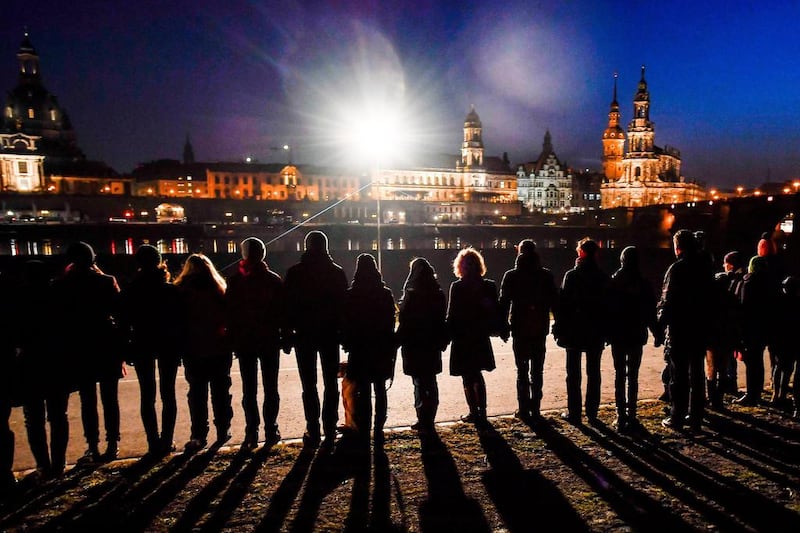 People join hands to form a human chain along the Elbe river opposite the Dresden skyline to commemorate the destruction of the city during World War II, in Dresden, Germany. Filip Singer / EPA
