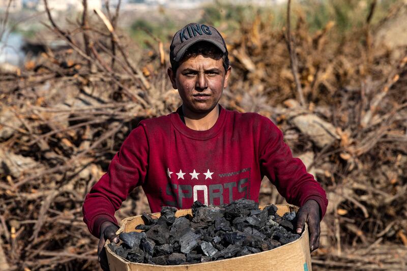 A worker carries a box of wood charcoal made for domestic use, in the countryside of Raqa in northern Syria, on November 23, 2022 (Photo by Delil SOULEIMAN  /  AFP)
