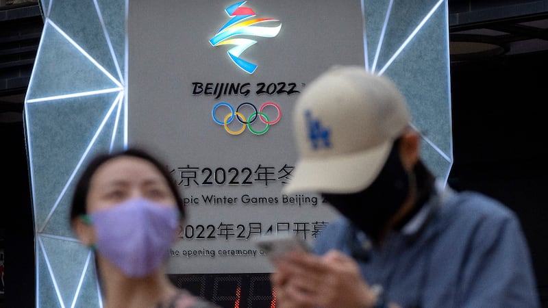 People wearing face masks to protect against Covid-19 walk past a display showing a countdown clock to the Beijing 2022 Winter Olympics in China. AP