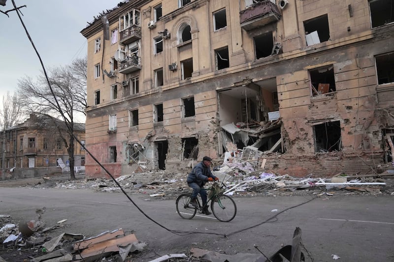 A man rides a bicycle in front of an apartment building that was damaged by shelling in Mariupol. AP