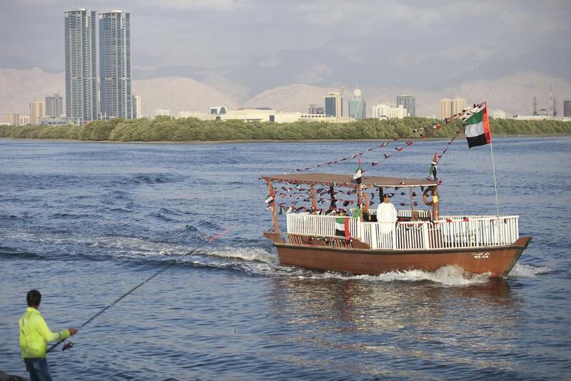 A boat decorated with UAE flags passes a fisherman in RAK. Reem Mohammed / The National