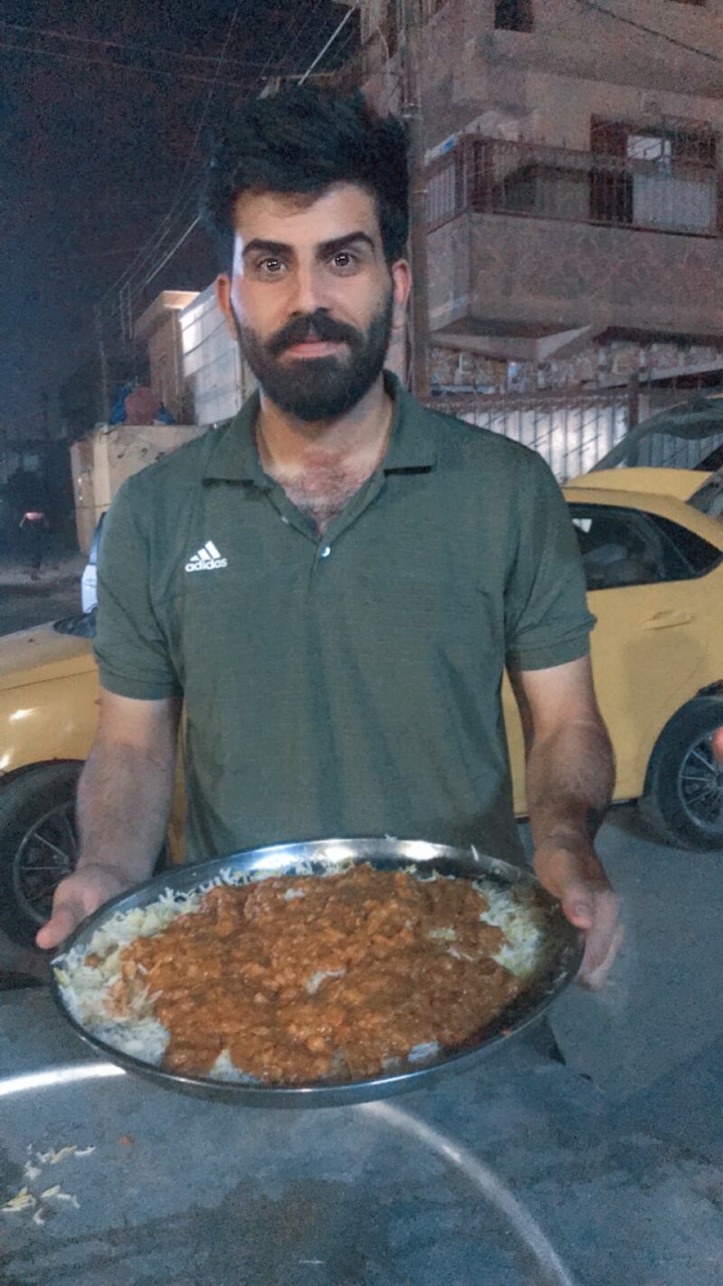 Muntadhar Hussein, 26, founder of Timman and Qeema in Ghazaliya Facebook group, holds a plate of a thick chickpea and diced meat stew – locally known as Qeema – which is served with rice at the event. Photo: Muntadhar Hussein.