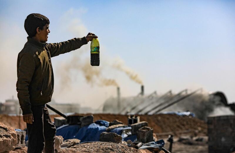 A boy holds up a bottle of oil at a makeshift refinery near Tarhin, in Aleppo, Syria. AFP
