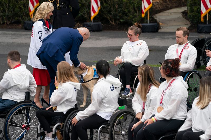 President Joe Biden and first lady Jill Biden stop to pet a service dog as they arrive for an event with US athletes. AP