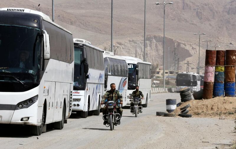 Syrian regime forces drive motorbikes past buses waiting at the entrance of Harasta in Eastern Ghouta, on the outskirts of Damascus, on March 22, 2018, after a deal was struck with the rebels in the area to evacuate the town.
The deal to evacuate mainly members of the hardline Islamist rebel group Ahrar al-Sham and their families was announced on March 21 and brokered by regime ally Russia.  / AFP PHOTO / Louai Beshara