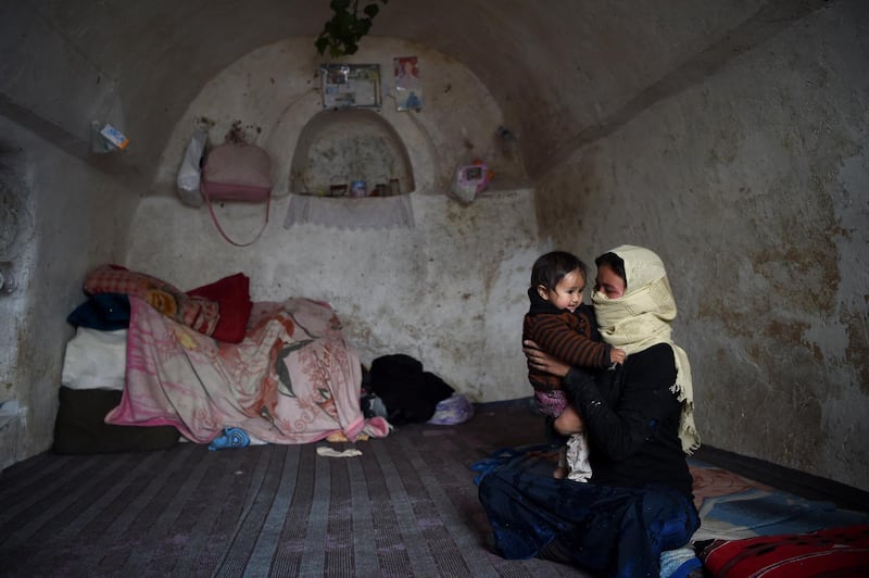 A Hazara woman holds her child inside a cave where they lives with their family at Tak Darakht village on the outskirts of Bamiyan province on March 6, 2021. (Photo by WAKIL KOHSAR / AFP)